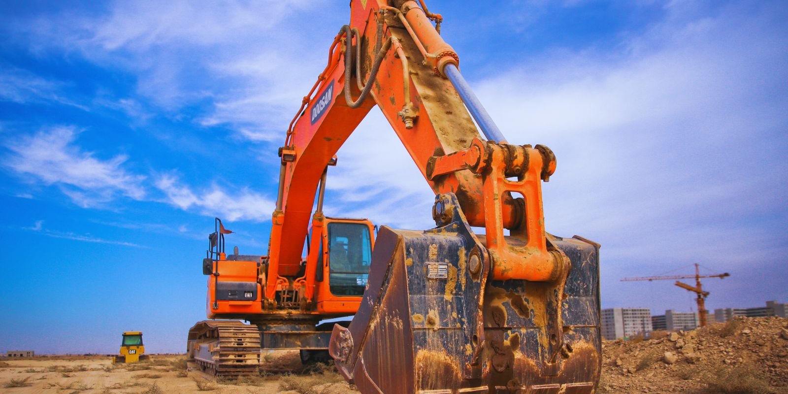 Excavadora de cadenas con el cazo en primer plano sobre un solar despejado