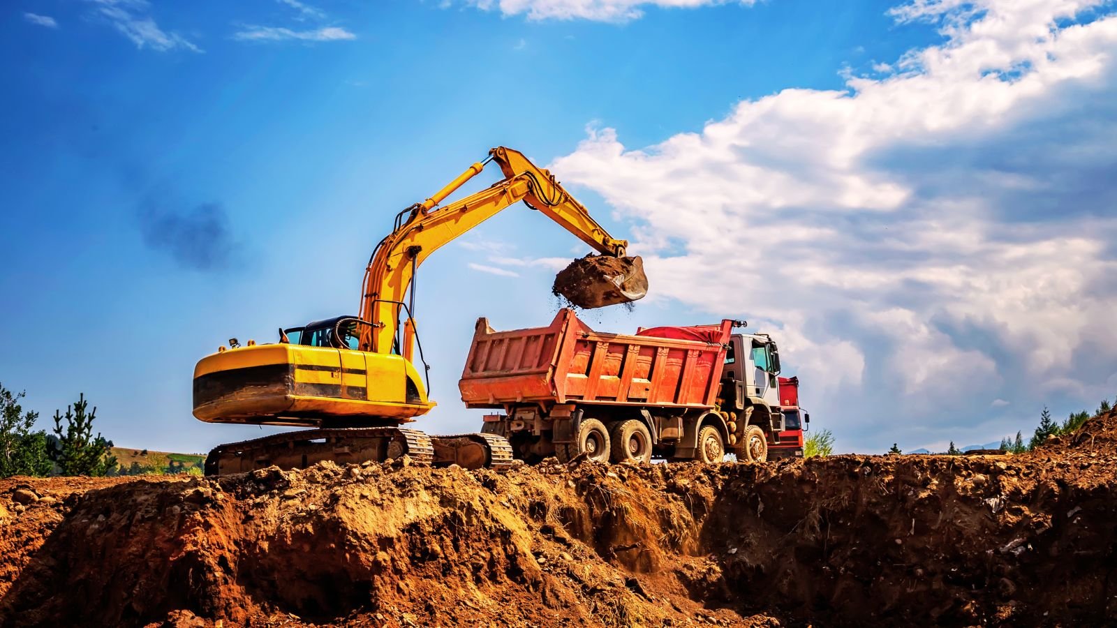 Excavadora de cadenas cargando tierra en un camión bañera durante el vaciado de un solar
